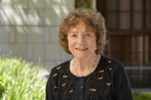 Barbara Babcock, an older woman in a dark shirt, smiling at the viewer with a campus building in the background.
