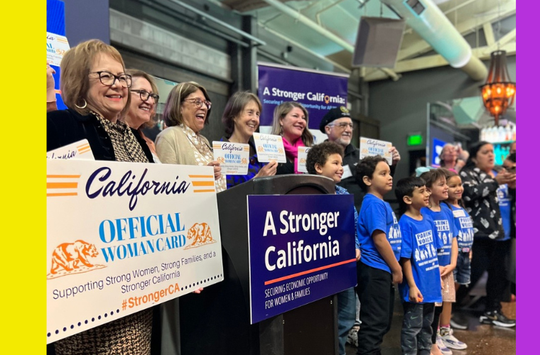 Image of lawmakers, advocates, children, smiling and holding up signs celebrating the Stronger California Advocates Network. They are lined up, this photo was taken to the left of them while they smile at another camera.