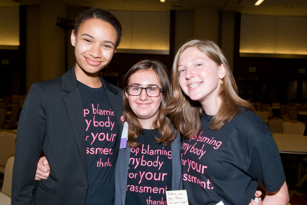 A photo of three girls wearing matching t-shirts that say "Stop blaming my body for your harassment. Thanks."